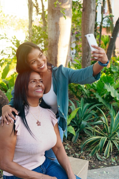 Photo joyeuse mère et fille africaines s'embrassant en prenant un selfie dans le parc