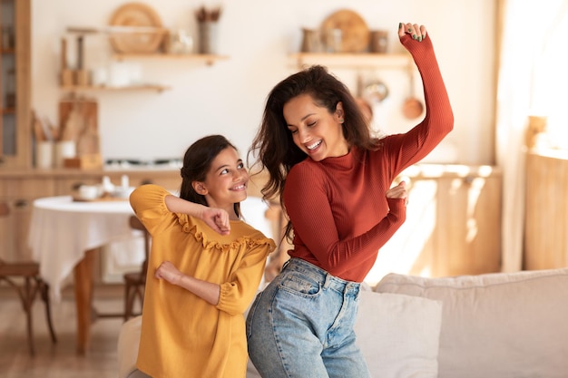 Joyeuse mère et fille bougeant et dansant sur de la musique à l'intérieur