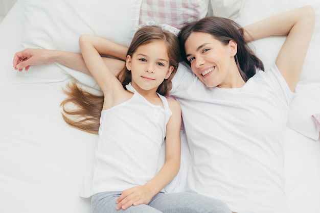 Joyeuse mère et fille embrassent comme s'allonger sur une literie blanche, se réveiller le matin