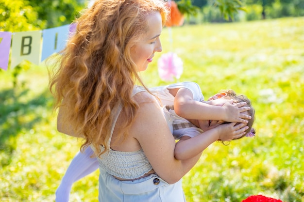 Joyeuse mère et fille s'amusant à l'anniversaire de l'enfant sur une couverture avec des décorations en papier dans le parc