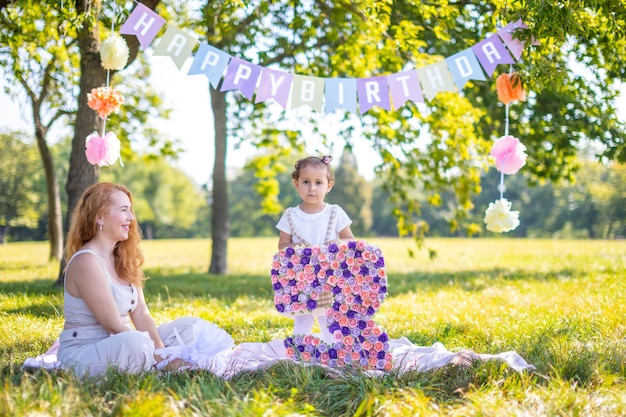 Joyeuse mère et fille s'amusant à l'anniversaire de l'enfant sur une couverture avec des décorations en papier dans le parc