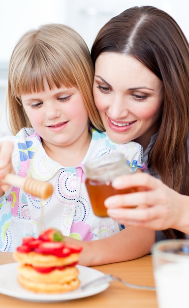 Joyeuse mère et sa fille mettant du miel sur des gaufres