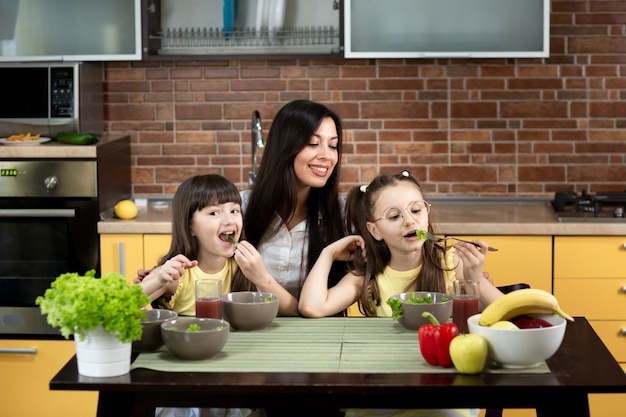 Joyeuse mère et ses deux filles mangent ensemble une salade saine à la maison