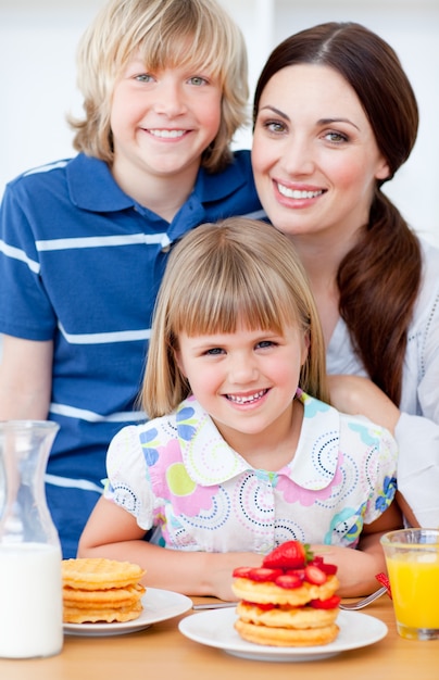 Joyeuse mère et ses enfants mangeant des gaufres avec des fraises