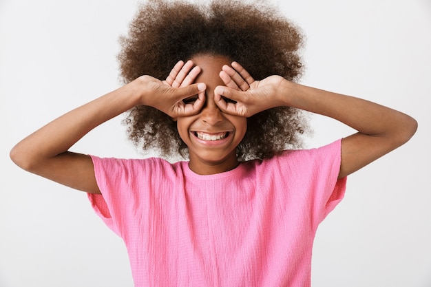 Joyeuse petite fille africaine drôle portant un chemisier rose debout isolé sur un mur blanc, grimaçant