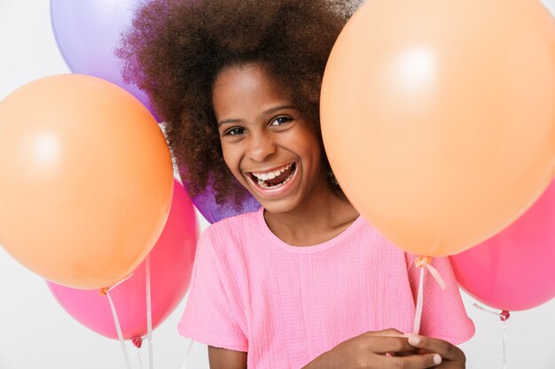 Joyeuse petite fille africaine portant un chemisier rose debout isolé sur un mur blanc, ayant une nageoire avec des ballons à air