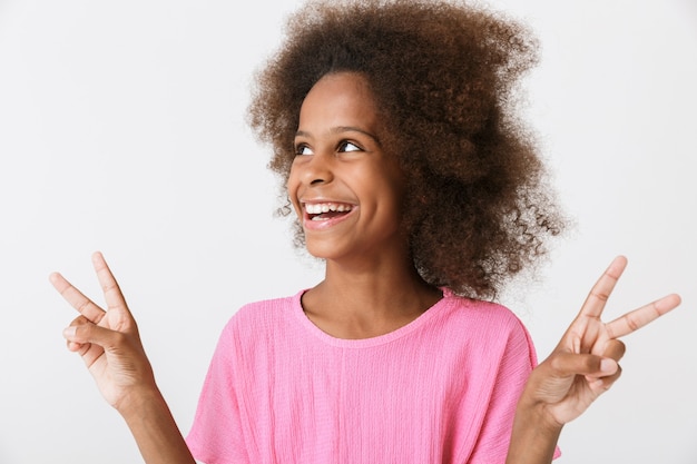 Joyeuse petite fille africaine portant un chemisier rose debout isolé sur un mur blanc, montrant un geste de paix