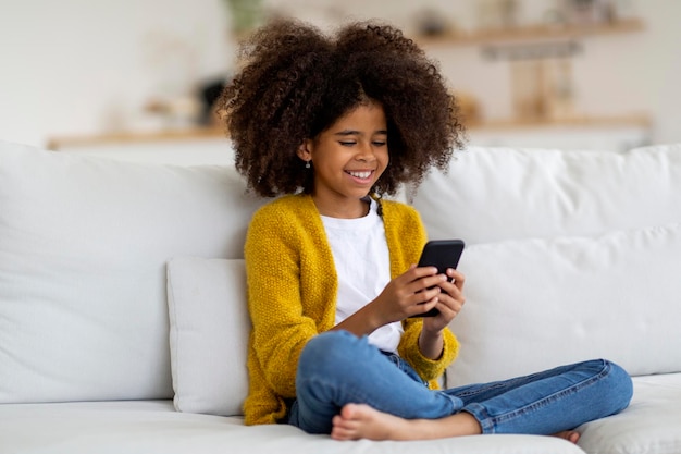 Joyeuse petite fille afro-américaine utilisant un smartphone à la maison