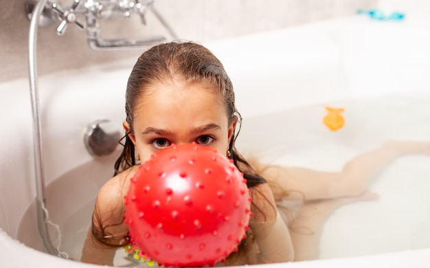Photo joyeuse petite fille charmante souriante baigne avec une boule rouge