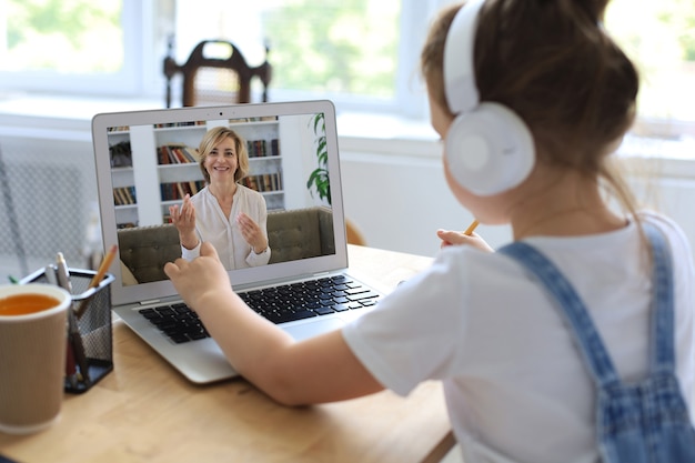 Photo joyeuse petite fille dans les écouteurs utilisant un ordinateur portable étudiant via un système d'apprentissage en ligne