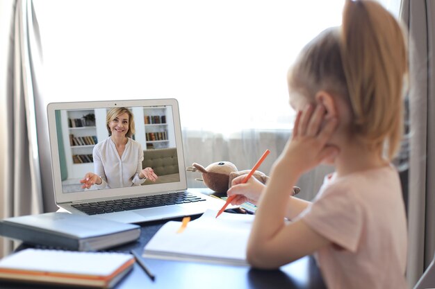 Joyeuse petite fille dans les écouteurs utilisant un ordinateur portable étudiant via un système d'apprentissage en ligne