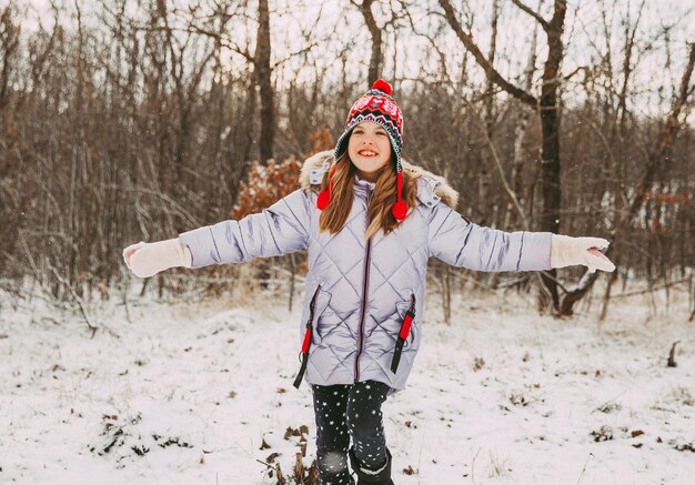 Joyeuse petite fille joyeuse s'amusant dans la forêt un jour d'hiver. l'enfant joue avec la neige.