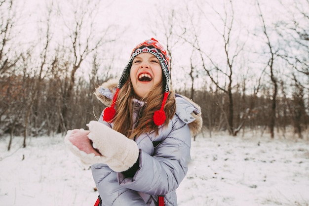 Joyeuse petite fille joyeuse s'amusant dans la forêt un jour d'hiver. l'enfant joue avec la neige.