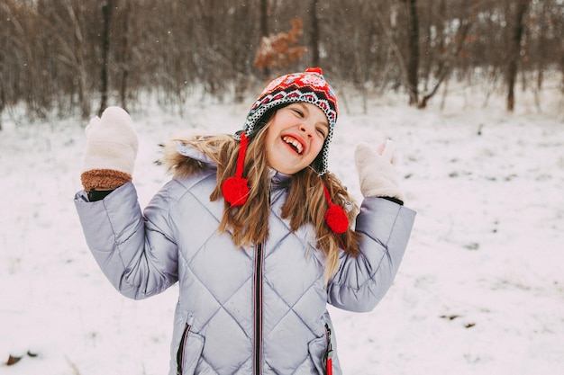 Joyeuse petite fille joyeuse s'amusant dans la forêt un jour d'hiver. l'enfant joue avec la neige.