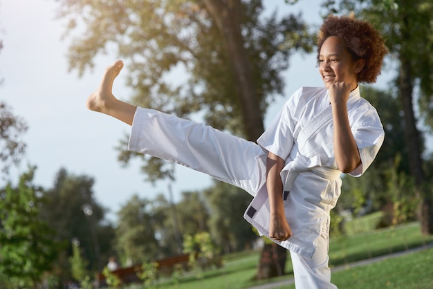 Joyeuse petite fille en kimono pratiquant le karaté dans la rue