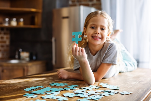 Joyeuse petite fille mignonne allongée sur la table tout en jouant avec des puzzles