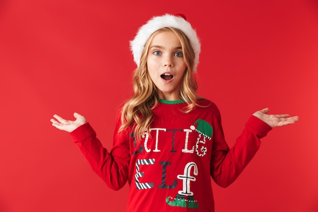 Photo joyeuse petite fille portant un chapeau de noël debout isolé, présentant un espace de copie