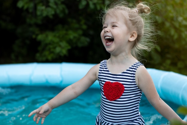 Joyeuse petite fille riante en maillot de bain rayé s'amusant dans la piscine, courant et nageant