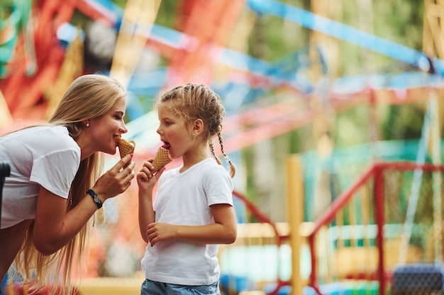 Joyeuse petite fille sa mère passe un bon moment dans le parc ensemble près des attractions