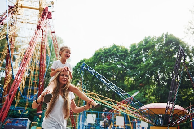 Joyeuse petite fille sa mère passe un bon moment dans le parc ensemble à proximité des attractions.