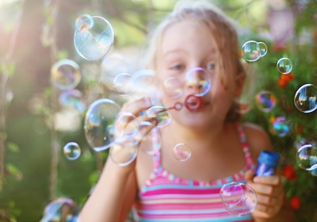 Joyeuse petite fille souffle des bulles de savon en plein air en été
