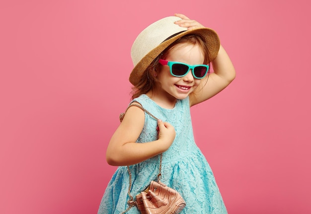 Joyeuse petite fille en vêtements de plage se dresse sur le rose isolé exprime la joie et le bonheur