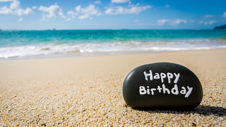 Joyeuse pierre d'anniversaire sur une plage de galets en face de la mer Célébration d'un anniversaire en vacances