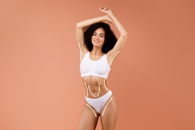 Joyeuse souriante belle jeune femme noire mince portant des sous-vêtements blancs démontrant son corps mince parfait avec des courbes parfaites sur fond beige studio, résultats du programme de perte de poids, collage
