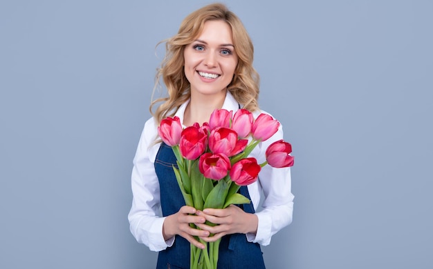 Joyeuse vendeuse de fleurs en tablier avec des fleurs de tulipes printanières sur fond gris