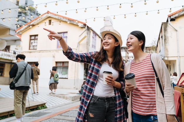 Joyeuses amies asiatiques marchant au marché aux puces à côté du vendeur debout dans la rue en plein air dans une petite ville. les jeunes femmes voyagent en russie shopping dans swap rencontrez le doigt montrant sur la lumière du soleil