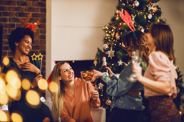 Joyeuses amies multiethniques s'amusant tout en portant un toast avec du champagne lors de la fête à la maison de Noël ou du Nouvel An ensemble.