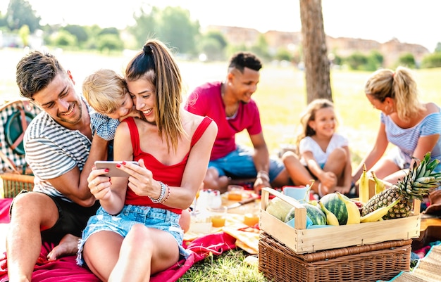 Joyeuses familles multiethniques jouant avec un téléphone à la garden-party pic nic