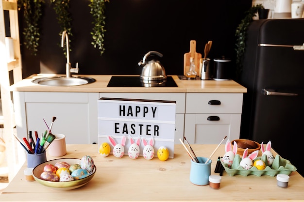 Joyeuses félicitations de Pâques sur la table, oeufs colorés peints à côté, dans la cuisine à l'intérieur. Préparation au concept de vacances de Pâques à la maison.