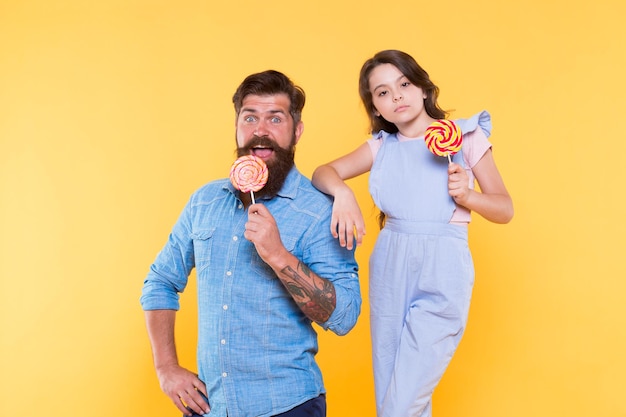 Joyeuses fêtes Douce enfance Quand les enfants semblent difficiles à satisfaire La fille et le père mangent des bonbons sucrés Homme barbu et mignon bébé doux Papa aimant et petite fille mangeant une sucette Vacances d'été