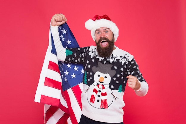 Joyeuses fêtes Joyeux Noël Saison des fêtes aux États-Unis Fier d'être un Américain Bonne année Joyeux père Noël célébrer Noël et le nouvel an Hipster barbu heureux souriant tenir le drapeau américain