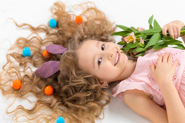 Photo joyeuses fêtes pâques enfants fille en lapin lièvre oreilles de lapin oeufs colorés dans les cheveux fleurs de printemps