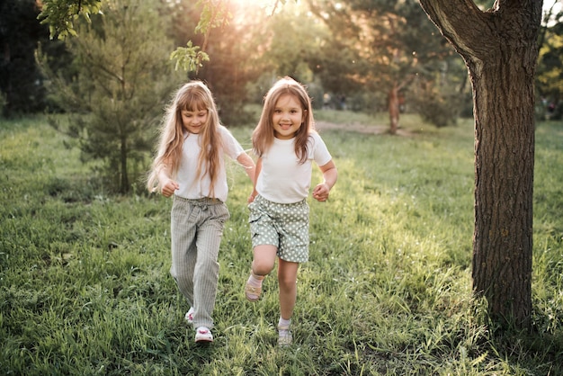 Joyeuses filles d'enfant de soeur gaie courant dans le parc ensemble sur l'herbe verte