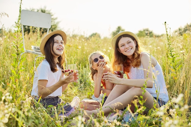 Joyeuses filles enfants mangeant une tarte aux fraises et buvant du thé avec des baies de menthe sur pique-nique, fond de prairie ensoleillée d'été. Vacances, enfance, amusement, concept d'été