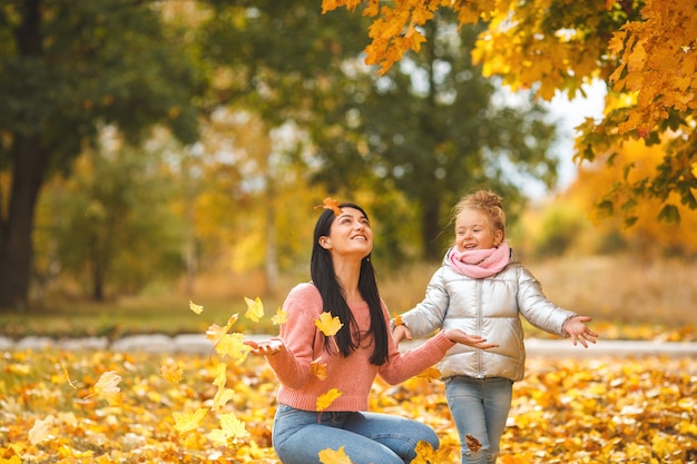 Joyeuses filles jouant avec des feuilles jaunes. Heureuse mère et petit enfant à l'automne s'amusant