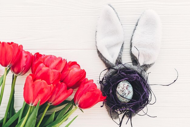 Joyeuses pâques concept oreilles de lapin et oeuf élégant dans le nid et les tulipes sur fond en bois blanc plat poser avec un espace pour le texte créatif image de pâques maquette de carte de voeux de la saison du printemps