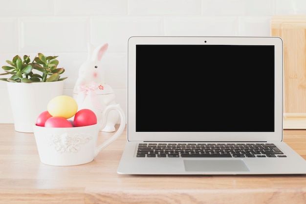 Joyeuses Pâques! Espace de travail avec ordinateur portable, oeufs de Pâques, lapin, succulentes sur le comptoir de la cuisine, gros plan. Ustensiles de cuisine à l'intérieur de la cuisine moderne. Carreaux blancs