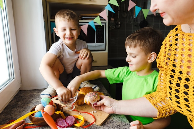 Joyeuses Pâques. Une grand-mère et ses petits-fils décore des pâtisseries. Héhé, préparation pour Pâques à la maison