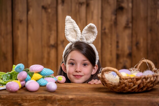 Joyeuses Pâques! Une jolie fille souriante regarde derrière la table.