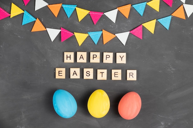 Joyeuses Pâques lettrage sur des carrés en bois à bord de la craie avec des œufs peints et guirlande de feutre coloré