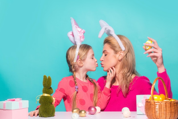 Joyeuses Pâques Une mère et sa fille peignant des oeufs de Pâques et s'embrassant Famille heureuse se préparant pour Pâques Mignonne petite fille enfant portant des oreilles de lapin le jour de Pâques isolée sur bleu