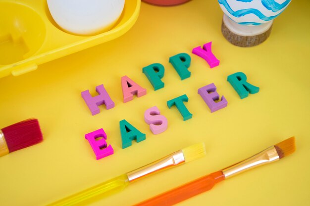 Joyeuses Pâques mot fait de lettres colorées avec des oeufs dans le bac à oeufs jaune, peintures et pinceaux paitning oeuf en vagues bleues sur jaune