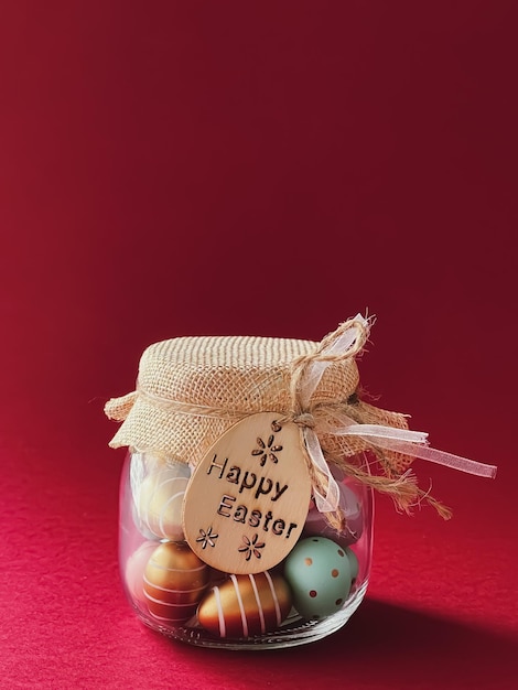 Joyeuses Pâques Oeufs de Pâques peints colorés dans un bocal en verre sur fond rouge Religion chrétienne et concept de vacances