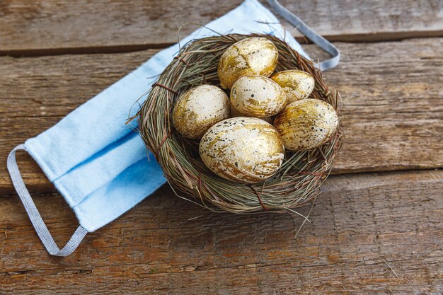 Joyeuses Pâques, préparation pour les vacances. Oeufs de Pâques décorés d'or dans le nid avec masque de protection du visage sur fond de bois