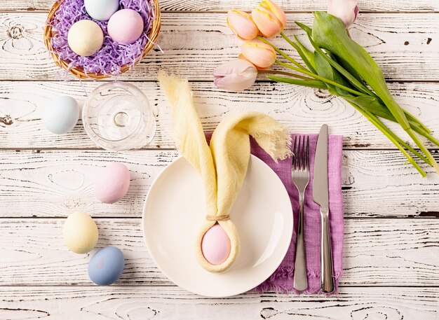 Joyeuses Pâques Réglage de la table pour la fête de Pâques Oeufs de Pâques lapin tulipes et couverts vue de dessus à plat sur fond rustique blanc