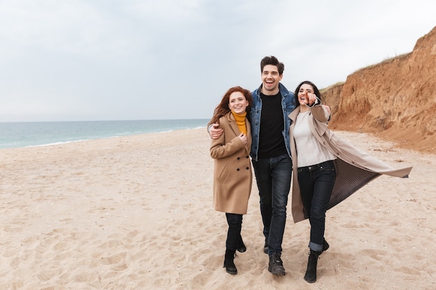 Joyeux amis marchant au bord de la mer en automne